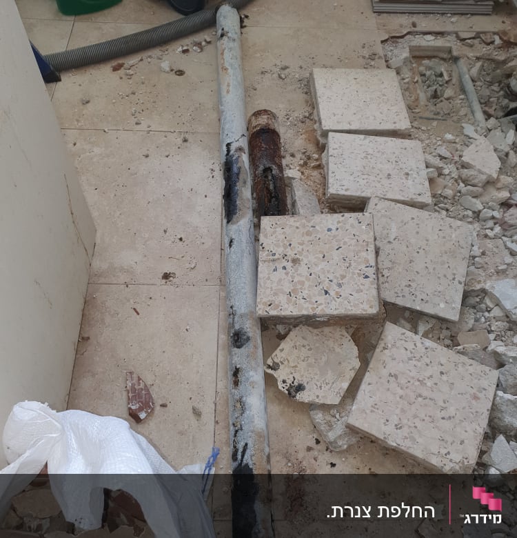 צינור חלוד על רצפה עם אריחים שבורים